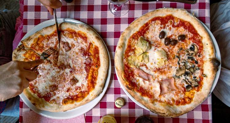 Deux pizzas sur une nappe à carreaux avec des mains qui atteignent les tranches.