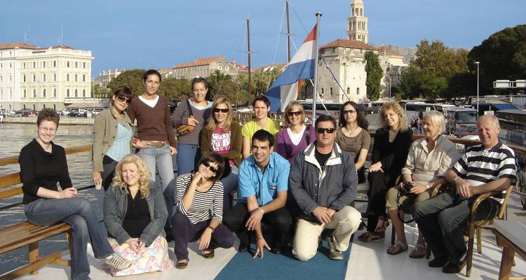 Grupo de personas posando en un barco con el telón de fondo de un pueblo.