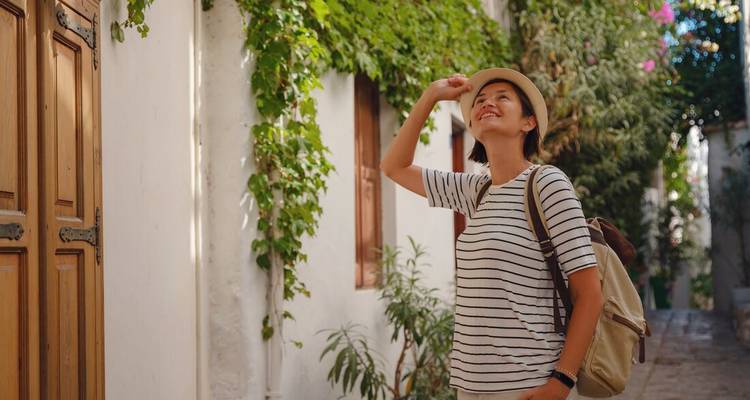 Female traveller in striped shirt and hat admires vine-covered whitewashed alley in coastal Turkey