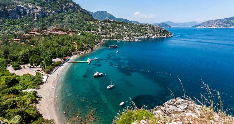 Stunning turquoise bay with boats, pebble beach and forested mountains near Marmaris on a clear summer day