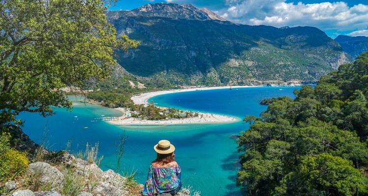 Traveller in floral dress and straw hat gazes over the stunning blue lagoon of Oludeniz from a cliff viewpoint