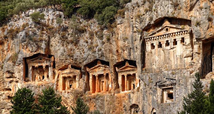 Ancient Lycian rock tombs carved into steep cliff faces above treetops near Dalyan