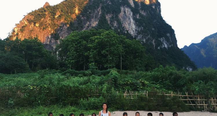 Un grupo de niños y un adulto de pie junto a una montaña de exuberante vegetación.