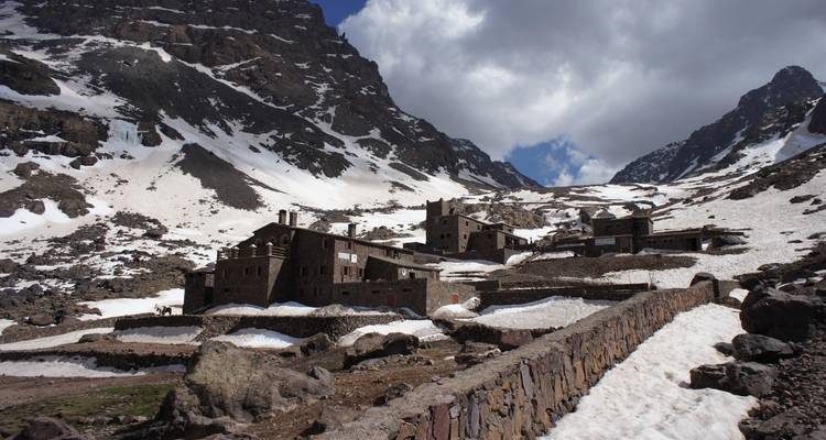 Albergue de montaña enclavado entre picos nevados bajo un cielo nublado.