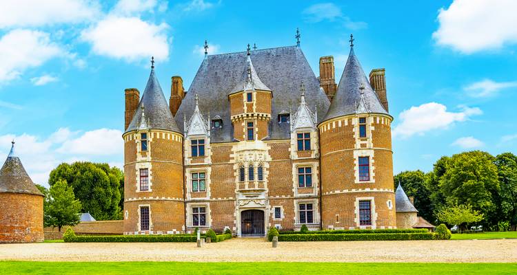 Impressionnant château Renaissance en brique et pierre aux tours coniques se dressant sur un ciel bleu et une pelouse impeccablement entretenue.