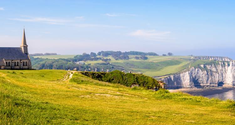 Clifftop chapel overlooking dramatic white chalk cliffs and the English Channel under clear morning sky.
