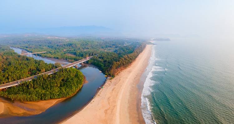 Vue aérienne d'une plage avec une rivière et un pont, entourée de verdure