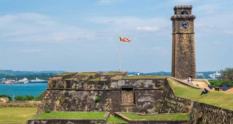 Stone fortress with clock tower overlooking a harbor.