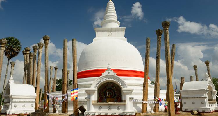 Un grand stupa blanc entouré de piliers anciens sur un ciel bleu.