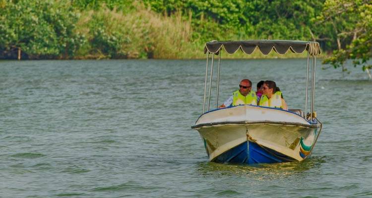 Small boat with people on a river, with dense vegetation on either side.