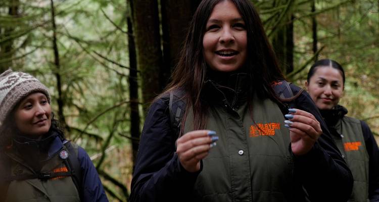 Un guía indígena habla con los visitantes en una selva tropical templada cubierta de musgo y niebla.