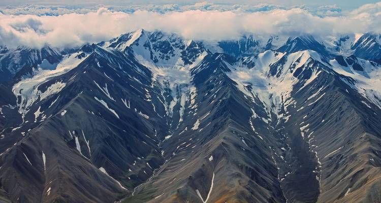 Vista aérea de montañas accidentadas con crestas afiladas, salpicadas de nieve bajo una capa de nubes.