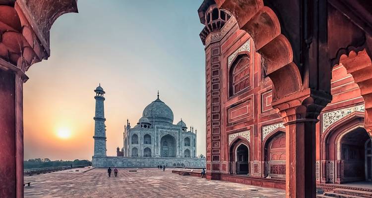 The Taj Mahal at sunrise viewed through an ornate archway.
