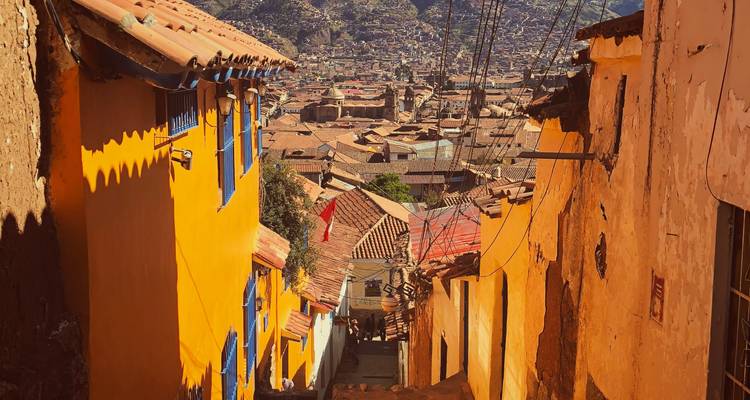 Une ruelle escarpée colorée bordée de maisons aux teintes jaune vif et orange avec des cadres de fenêtres bleus surplombant une ville andine historique.