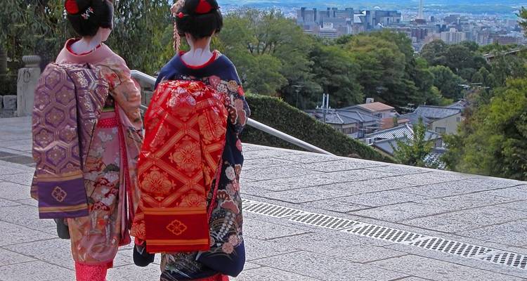 Deux femmes vêtues de kimonos traditionnels colorés et de ceintures ornées marchent le long d'un chemin pavé de pierre avec vue sur Kyoto.