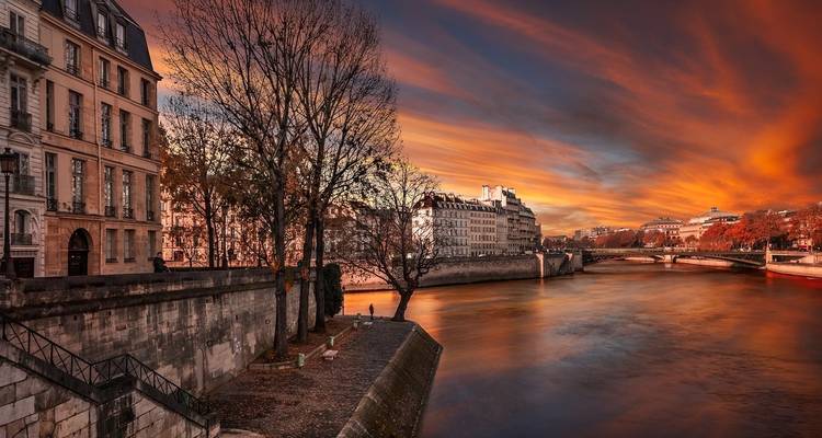 Escena fluvial en París durante el atardecer con árboles y edificios.