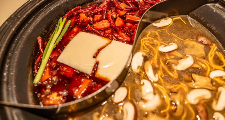 Fondue chinoise aux deux saveurs avec bouillon rouge épicé et soupe aux champignons claire divisés dans un pot en métal.