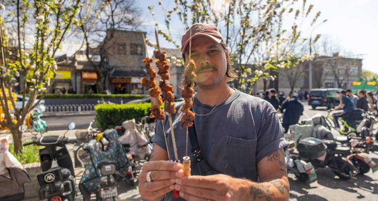 Le voyageur tient fièrement des brochettes de viande grillée dans une rue animée de Pékin.