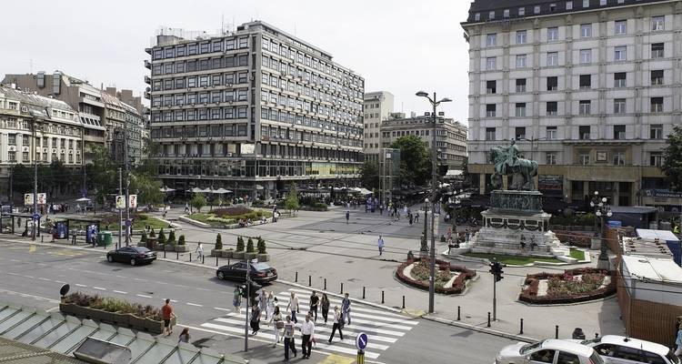 Una plaza de la ciudad bulliciosa con edificios modernos y un monumento histórico.