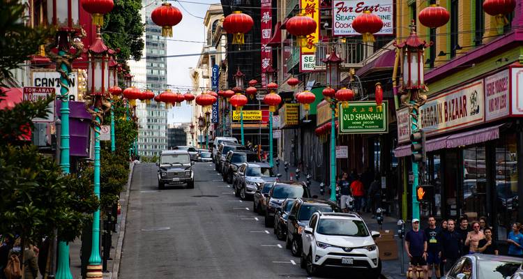 Belebte Straße in San Franciscos Chinatown, geschmückt mit roten Laternen über Reihen geparkter Autos.