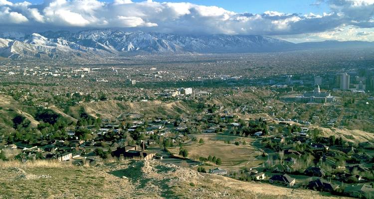 Expansive view over Salt Lake City suburbs toward snow-dusted Wasatch Mountains under scattered clouds.