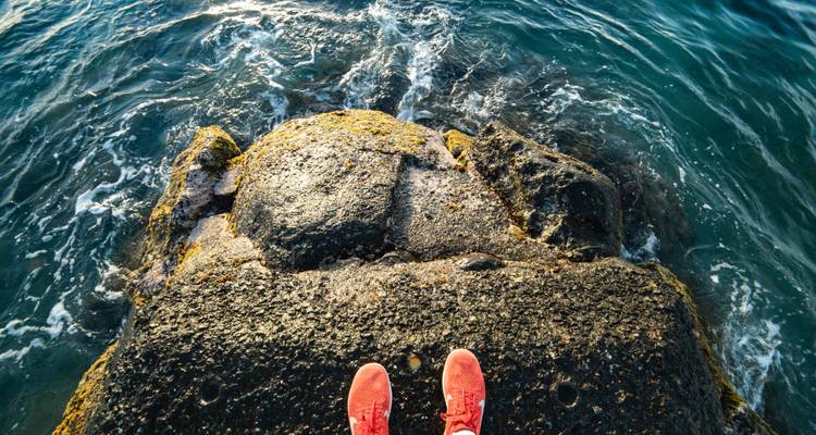 Gros plan de chaussures posées sur une surface rocheuse humide au bord de l'océan.