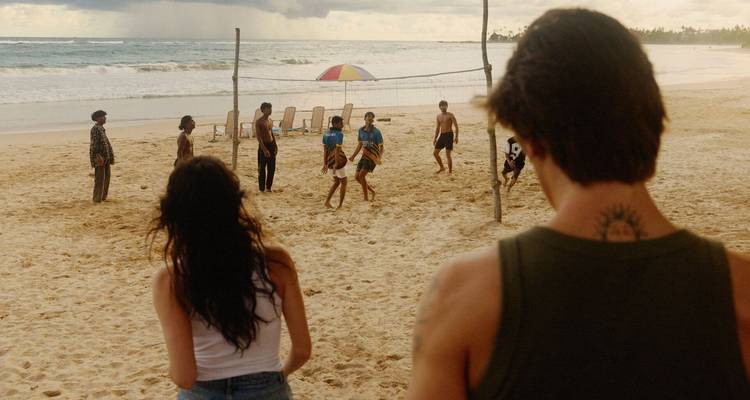 Les baigneurs jouent à un match de volleyball décontracté sur une large plage de sable tandis que deux personnes regardent au premier plan.