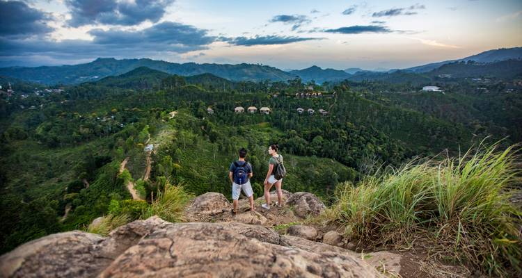 Wanderer stehen auf felsigem Felsvorsprung mit Blick auf sanft geschwungene grüne Berge