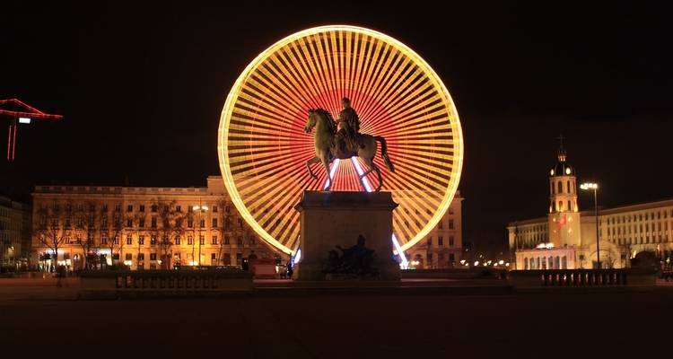 Une grande roue illuminée la nuit avec une statue au premier plan.