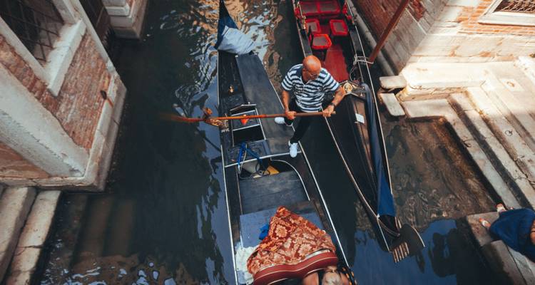 Un gondolero remando por un canal estrecho en Venecia.