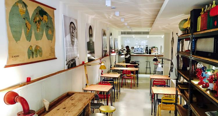 Acogedor interior de cafetería moderna con mapas del mundo, láminas de arte y mesas coloridas vacías