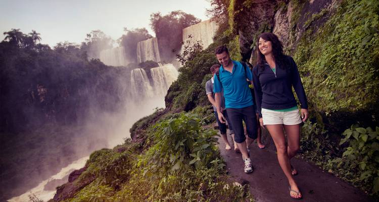 Los viajeros caminan por un sendero en la selva junto a la niebla de las imponentes Cataratas del Iguazú.