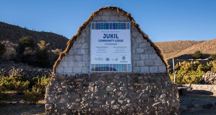 Panneau en pierre pour le Jukil Community Lodge surmonté de chaume sur un ciel bleu dégagé