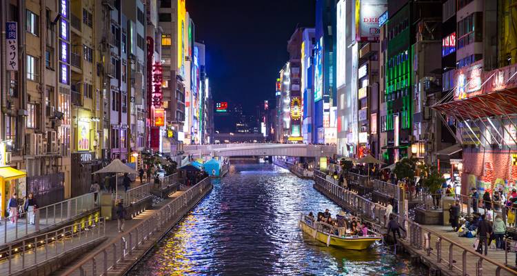 Canal illuminé de néons colorés de Dotonbori à Osaka la nuit avec un bateau de tourisme et des foules le long de l'eau.