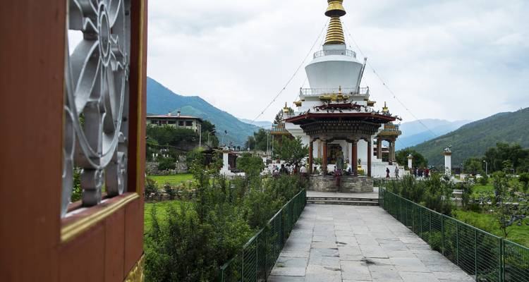 People visiting a stupa surrounded by green landscape.