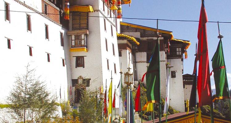 Exterior wall of Punakha Dzong with colourful prayer flags in foreground under clear sky