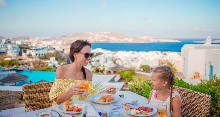 Mère et fille savourant un petit-déjeuner en plein air avec vue sur une ville insulaire blanchie à la chaux et la mer