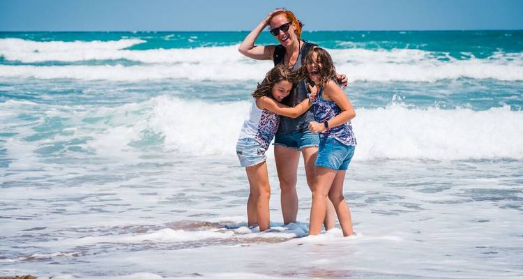 Une mère et deux filles riant ensemble dans les vagues d'une mer bleu éclatant
