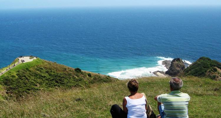 Mensen die op het gras zitten en uitkijken over de zee.