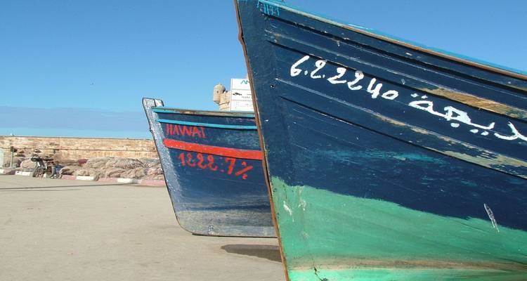 Primer plano de coloridos barcos de pesca de madera pintados de azul descansando en una rampa de puerto bajo cielos despejados.