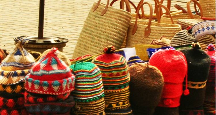 Sombreros tejidos de colores brillantes y canastas tejidas apiladas en un puesto de mercado con luz cálida.