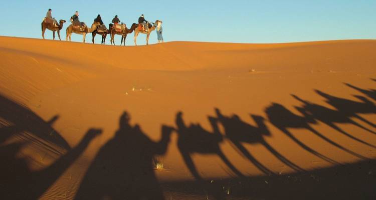 Gruppe von Menschen auf Kamelen, die Schatten auf die Sanddünen werfen.
