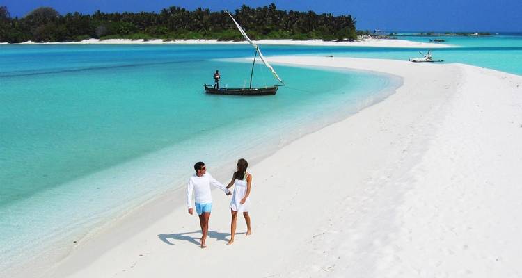 Young couple strolls hand-in-hand along a pristine white sandbar in the turquoise Maldives.