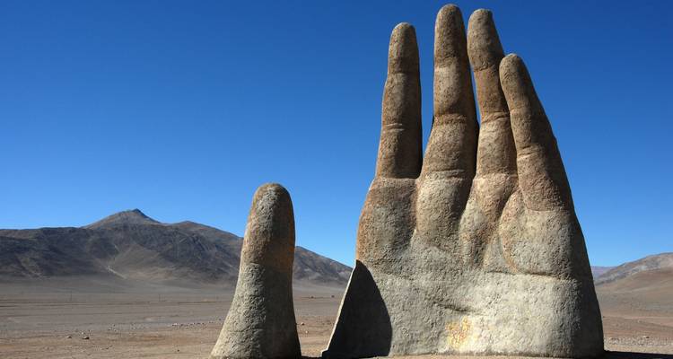 Grande sculpture de main en pierre dans un paysage désertique.