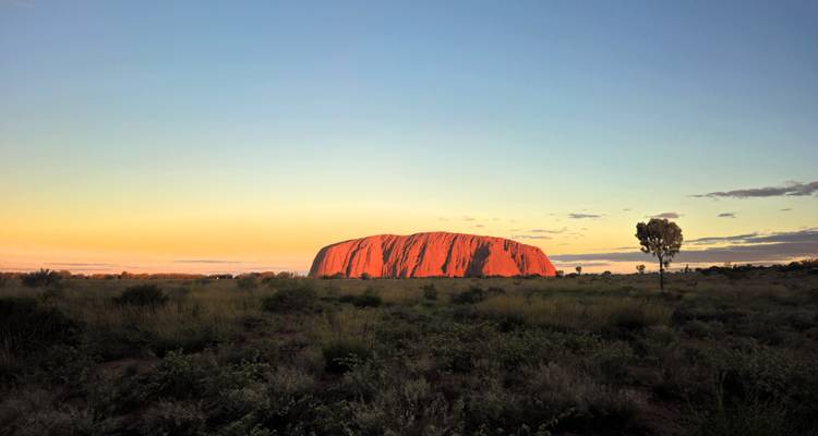 Uluru rougeoyant au coucher du soleil s'élevant au-dessus de la plaine désertique plate de l'Outback australien