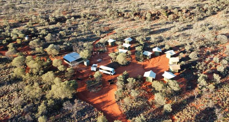 Vue aérienne d'un campement de brousse isolé aux sables rouges avec tentes et véhicules de soutien
