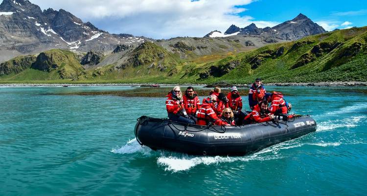 Zodiac-boot vol bundelde expeditiedeelnemers schiet over turquoise poolwateren met grillige bergen op de achtergrond