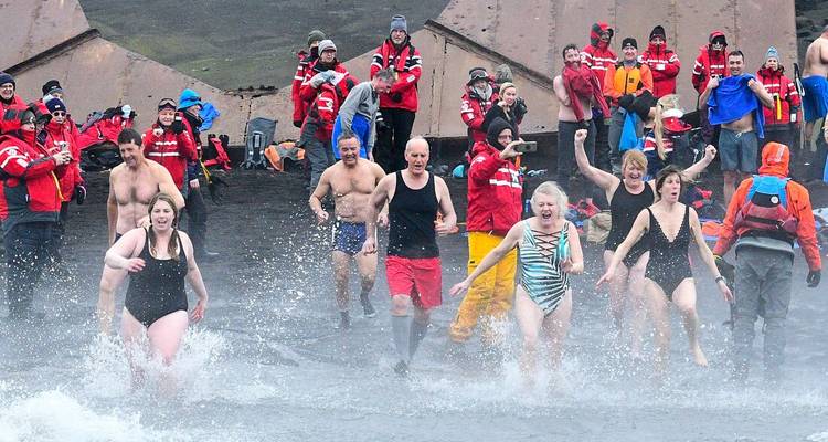 Juichende reizigers in badpakken rennen een steaming vulkanisch water in voor een ijzige duik terwijl toeschouwers toekijken