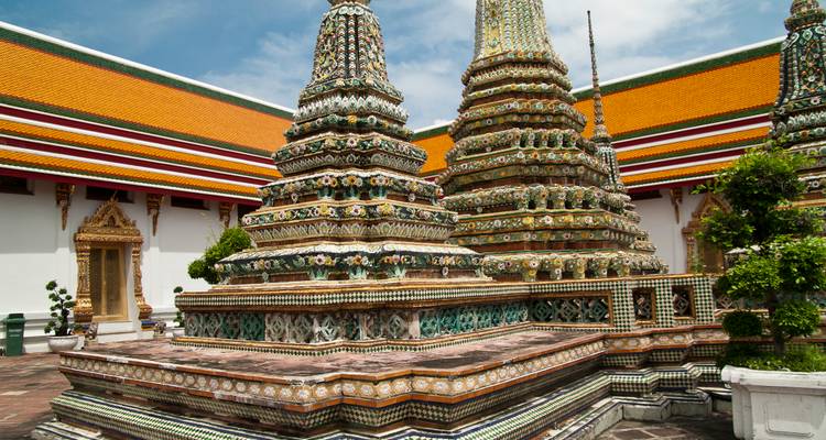 Stupas y agujas intrincadamente decoradas con azulejos en un patio de templo tailandés brillantemente iluminado bajo un cielo azul.