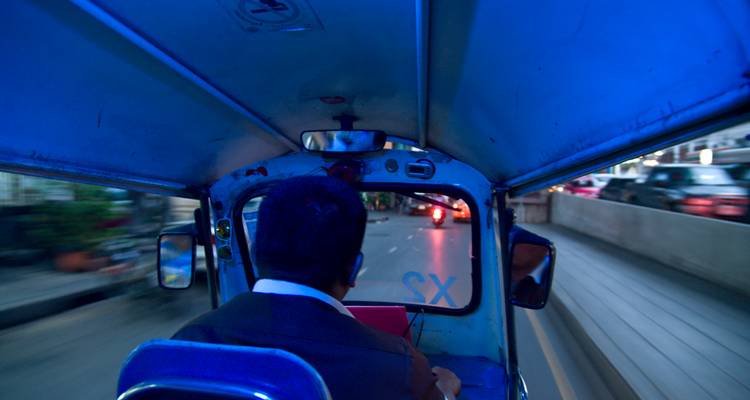 Vista desde el asiento trasero de un tuk-tuk en movimiento iluminado en azul mientras acelera por las calles de Bangkok de noche.